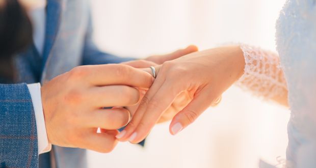 photo of a hand placing a ring on another hands ring finger 