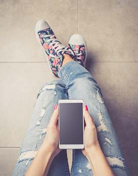View of lap, hands holding a cell phone